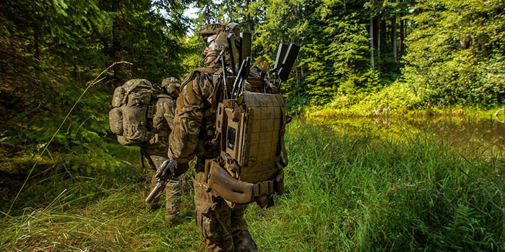 Soldiers with technology equipment walking through forest land